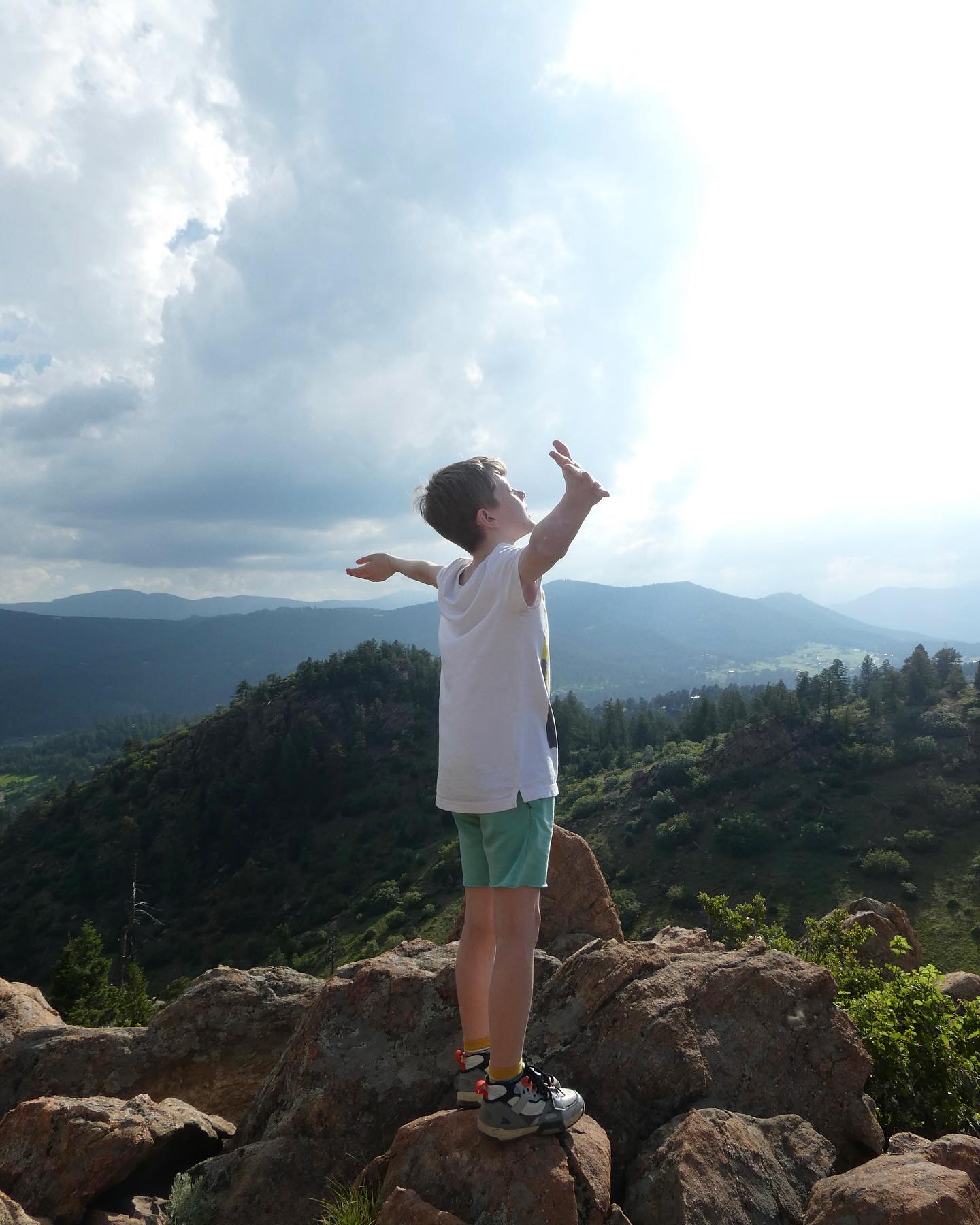 A picture of Oscar aged 9 standing on a rock on a mountain with his arms spread out looking at the sky.