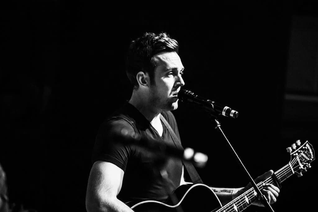 A black and white image of Rory singing and playing guitar, standing at a microphone.