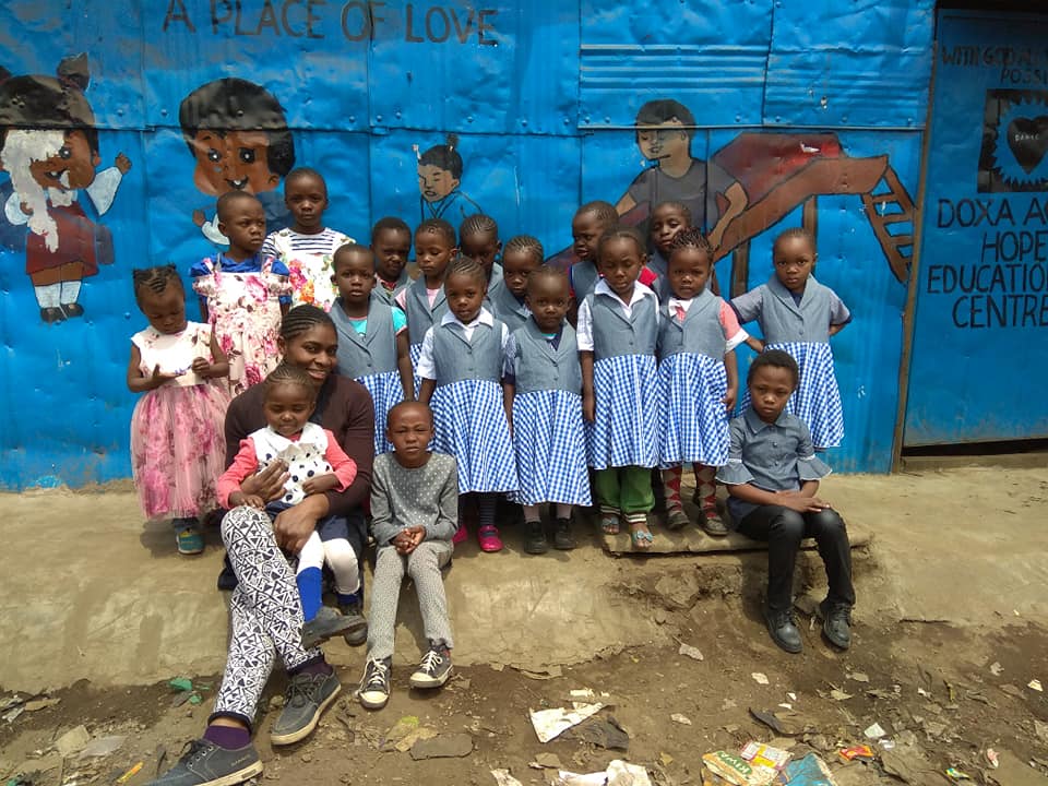 A colourful picture of a group of around 20 young children from kenya in school uniform standing infront of a blue wall