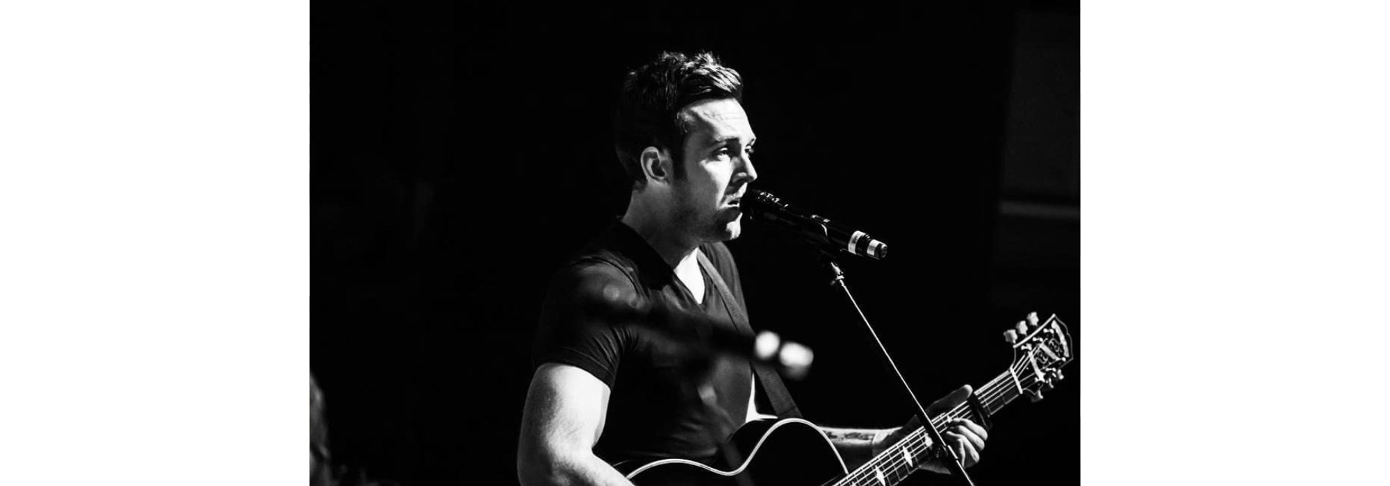 A black and white image of Rory singing and playing guitar, standing at a microphone. 